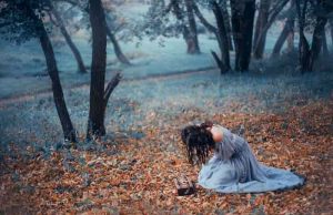 Ελπίδα. Το Φυλακισμένο Δώρο της Πανδώρας Ελπίδα. Μελαχρινή κοπέλα σε ένα μακρύ, ανοιχτό γκρι, ντεμοντέ φόρεμα, κάθεται στο κρύο έδαφος που καλύπτεται με Φθινοπωρινά πεσμένα φύλλα, σε ένα σκοτεινό δάσος, κλαίει πάνω από το ανοικτό κουτί της Πανδώρας