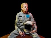 ΑΡΚΤΟΥΡΙΑΝΟΙ, ΤΕΛΟΣΙΑΝΟΙ, ΛΥΡΙΟΙ, ΑΓΓΕΛΟΙ γυναίκα με διαστημική στολή, κρατάει κράνος και λουλούδι, κάθεται σε ένα πλανήτη