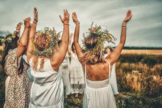 γυναίκες ντυμένες στα λευκά και με λουλουδένια στεφάνια στα μαλλιά υψώνουν τα χέρια στον ουρανό