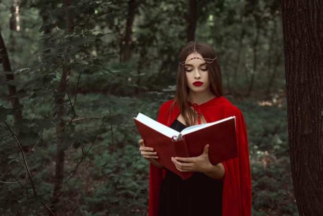 Κοπέλα με κόκκινο μανδύα διαβάζει βιβλίο με κόκκινο εξώφυλο που κρατάει με τα δάχτυλα των χεριών της